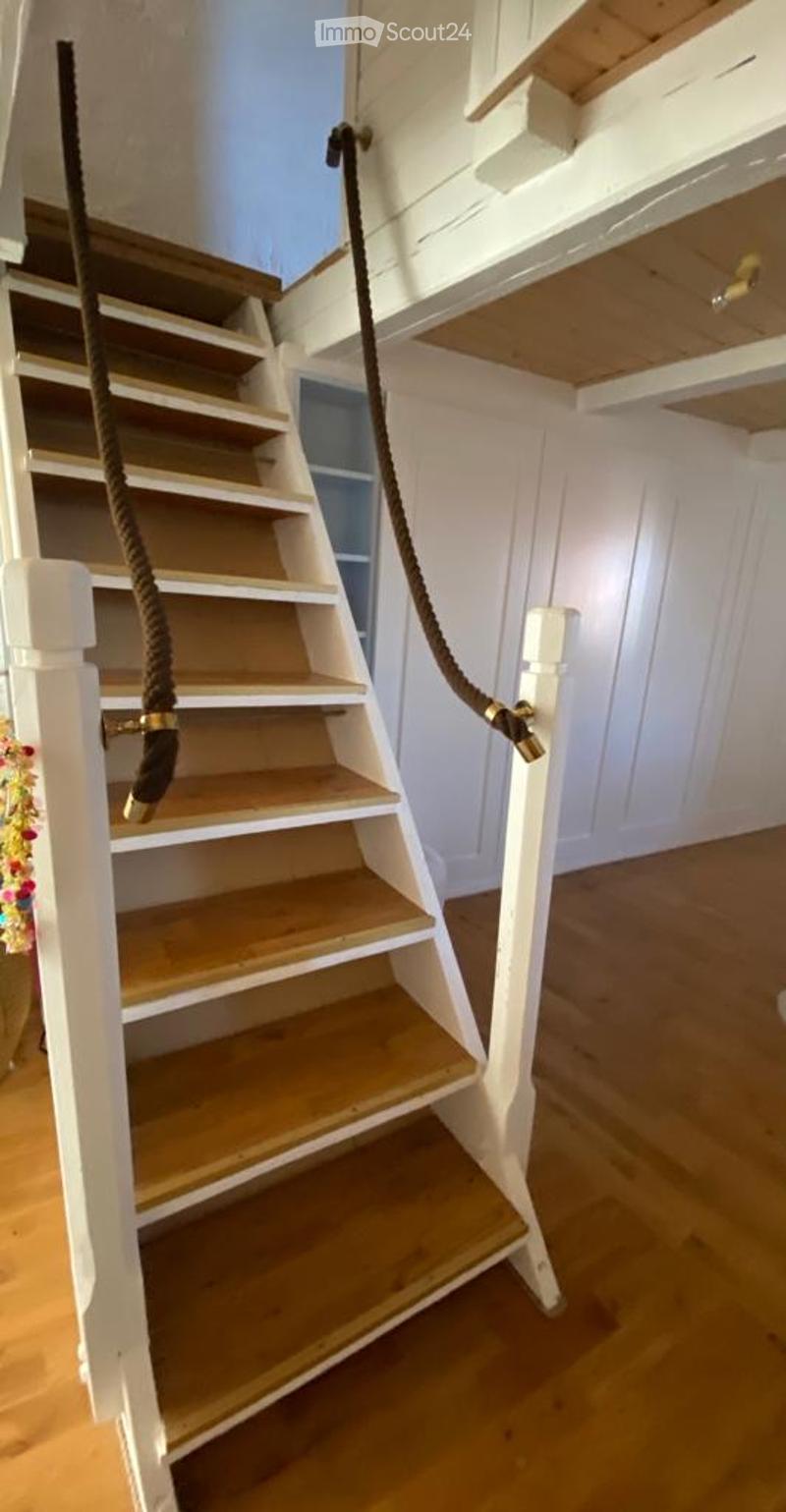 Wooden staircase with white railings and rope handrails, leading to an upper level with exposed wooden beams and white paneling.