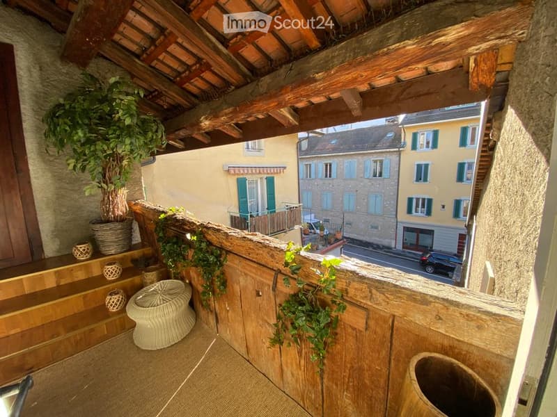 Wooden balcony with tiled floor, wooden railing, potted plants, and a view of the street and neighboring buildings.
