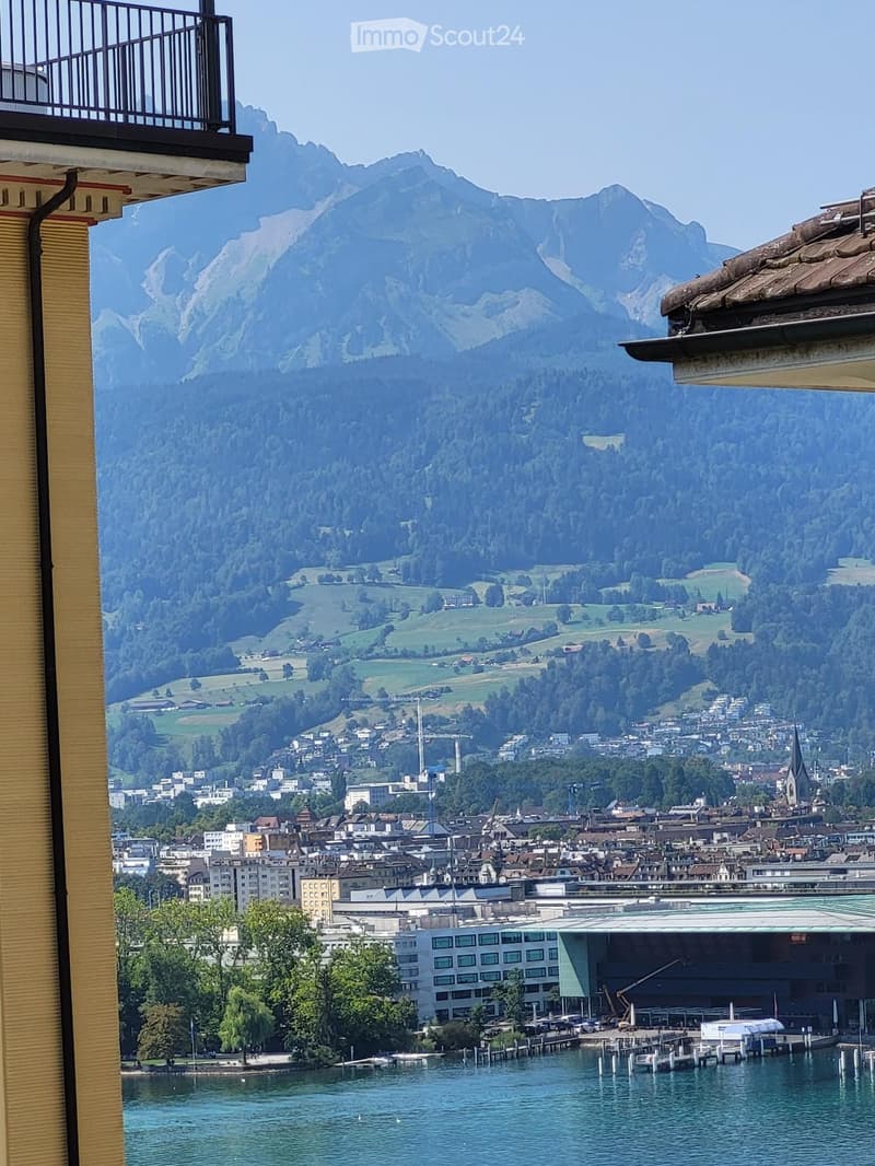 Balcony view overlooking a town, lake, and mountains with a clear blue sky.