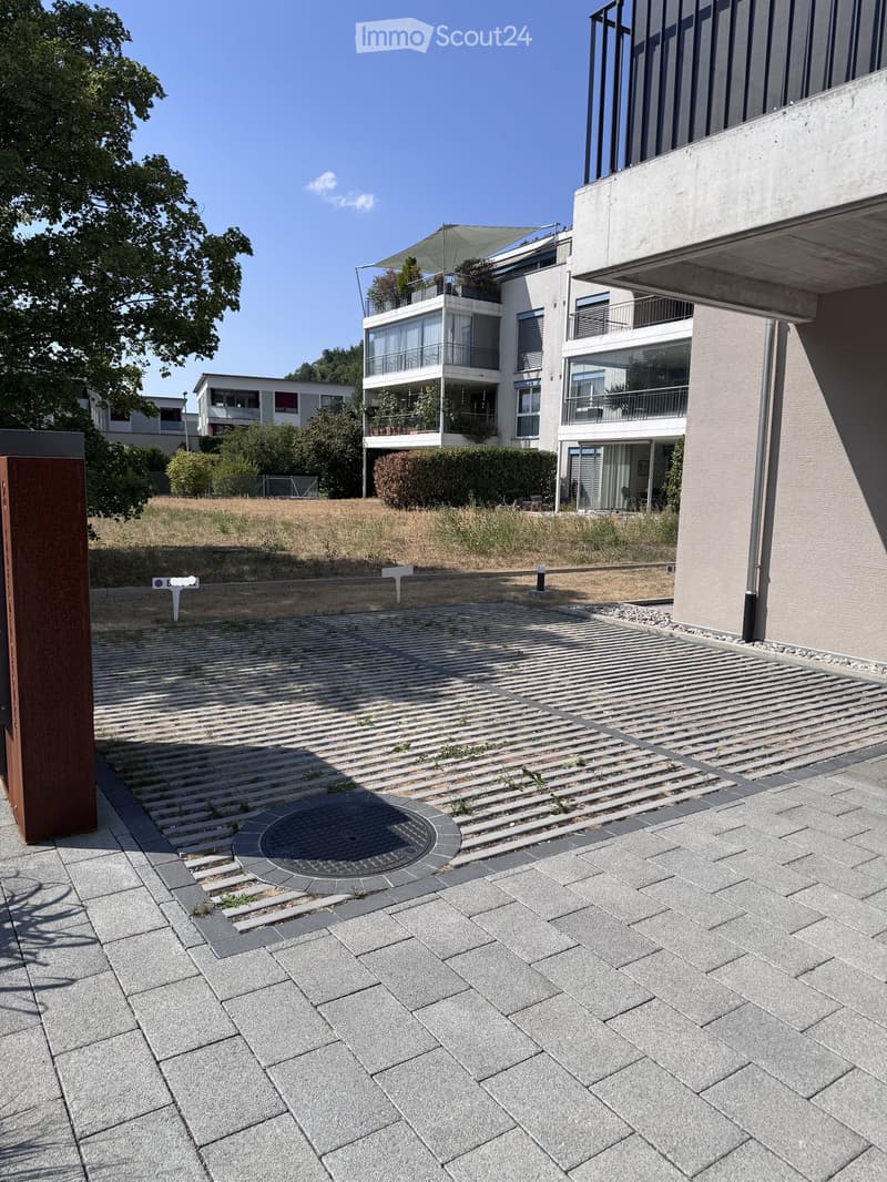 Modern outdoor area with paved stone tiles, raised ground floor, and contemporary building in the background.