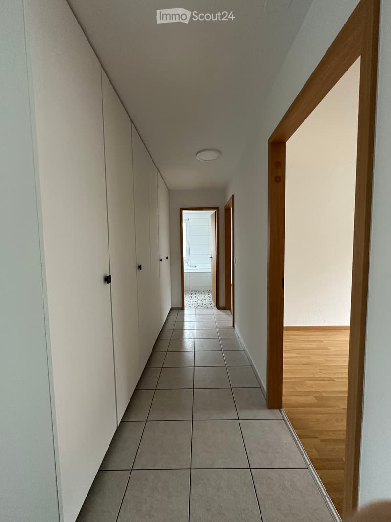 A narrow hallway with tiled flooring, white walls, and wooden doors leading to other rooms.
