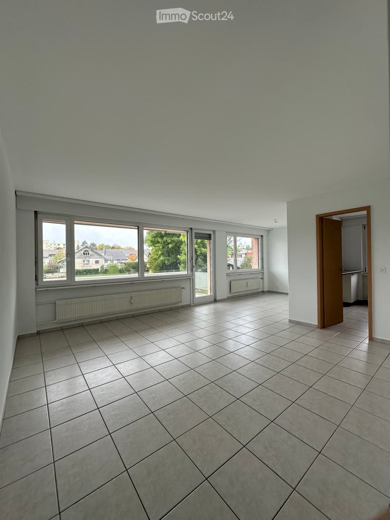 Empty room with tiled floor, large windows, and a door leading to another room.