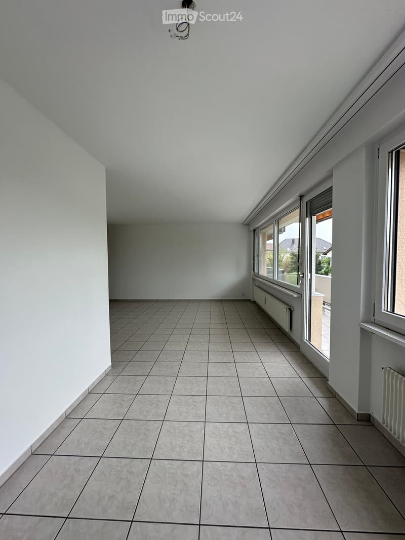 Empty room with tiled floor and white walls, featuring large windows and radiators.