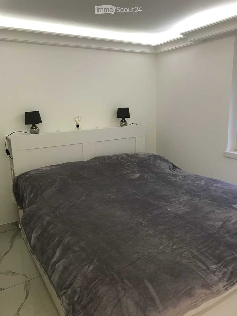 Modern bedroom with a large bed, dark bedding, bedside tables with lamps, and decorative items on top.