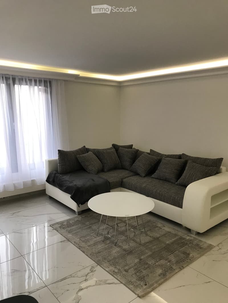 Modern living room with a white sectional sofa, dark cushions, a white coffee table, and a grey area rug on a marble floor.