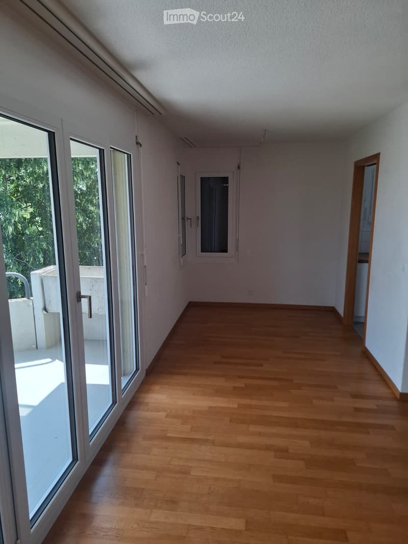 Empty room with wooden flooring, large windows, and a door leading to another space.