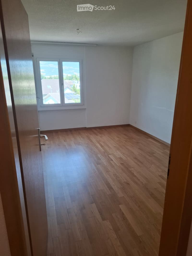 Empty room with wooden flooring, white walls, and a large window with a view of the outside.