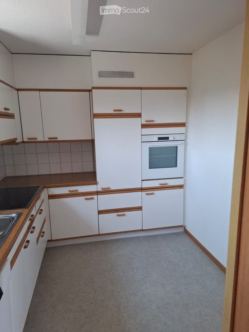 Modern kitchen with white cabinets, wooden trim, and a built-in oven. Features a countertop with a sink and a tiled backsplash.