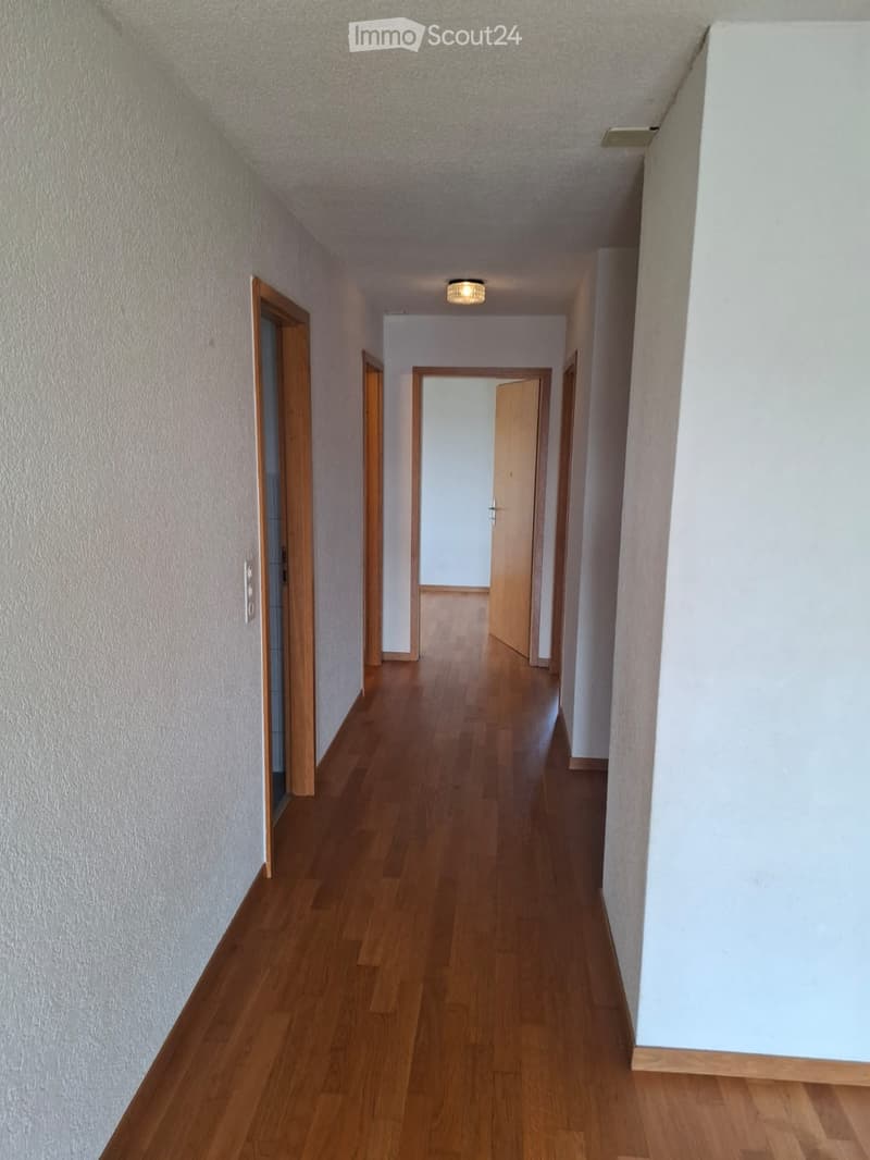 A long, narrow hallway with wooden flooring and white walls, featuring several open doors leading to other rooms.