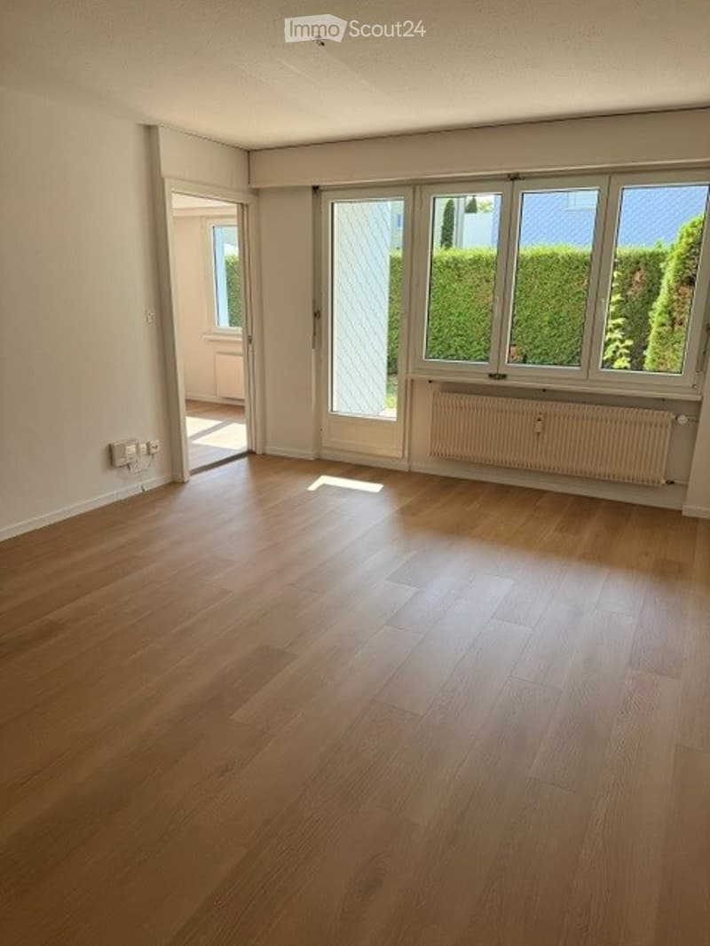 Empty room with wooden flooring, large windows, and a radiator. No furniture or equipment present.