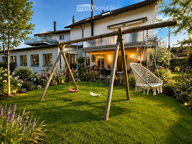 Well-maintained garden with a swing set, hanging chair, and patio area with outdoor furniture. The house features a balcony and large windows.
