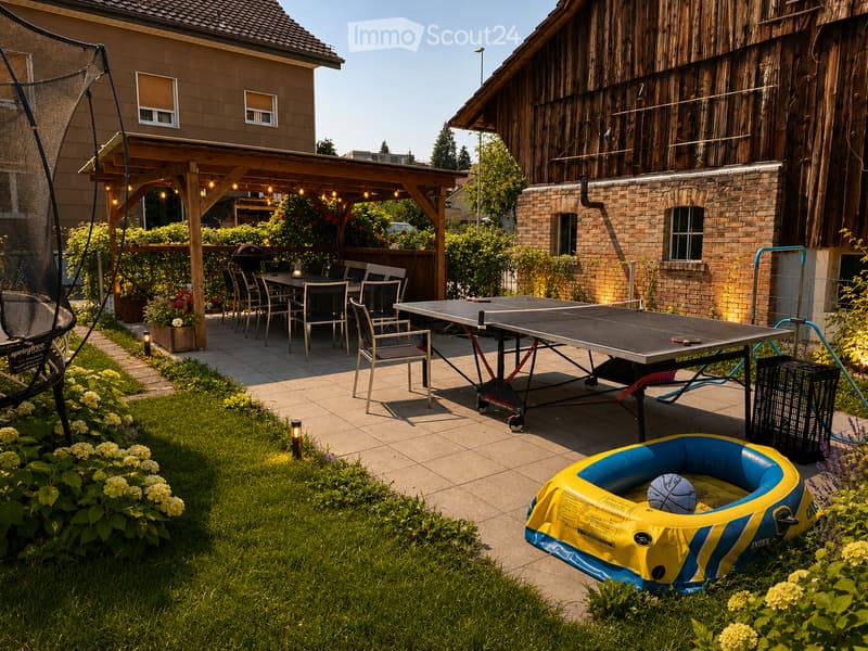 Outdoor patio area with a ping pong table, chairs, a small inflatable pool with a ball, and a covered seating area with additional chairs and a table.