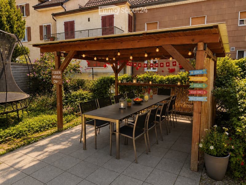 A covered outdoor patio with a wooden pergola, string lights, a dining table with chairs, a lantern, a bowl of fruit, and potted plants. Signs with messages like "BEACH" and "SUNSHINE" are visible.