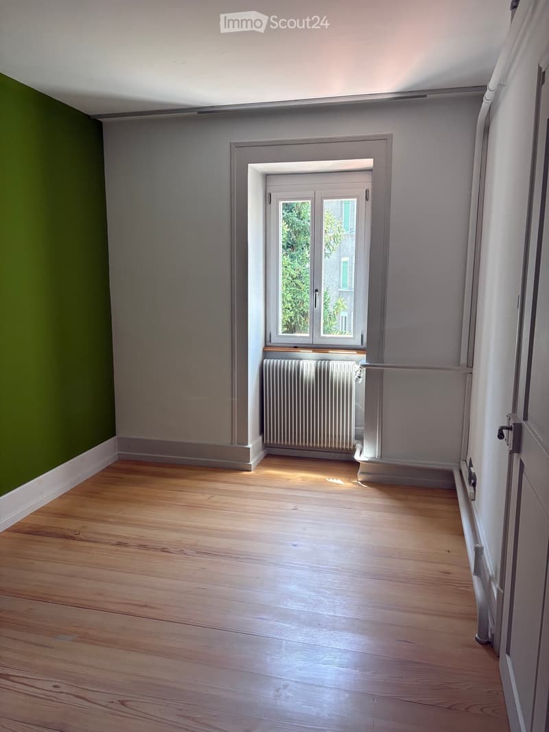 Empty room with wooden flooring, grey walls, a radiator, and a window with double glass panes.