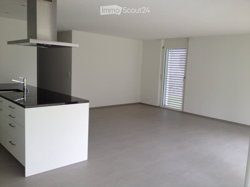 Empty kitchen with white cabinets, black countertop, and a modern faucet. The space features tiled flooring and a large window with blinds.