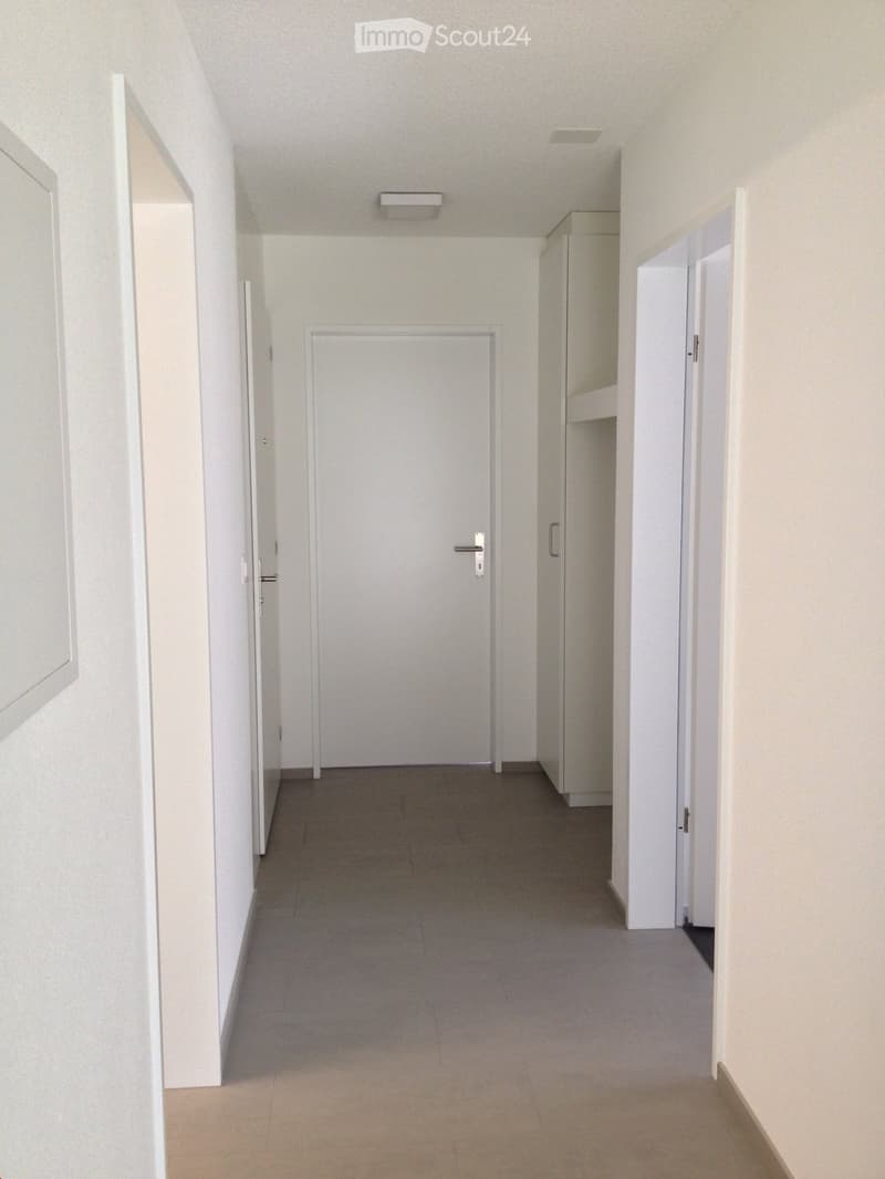 Empty hallway with white walls, tiled floor, and several closed doors.