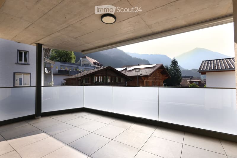Modern balcony with white tiled floor, sleek white railing, and a view of surrounding houses and mountains.