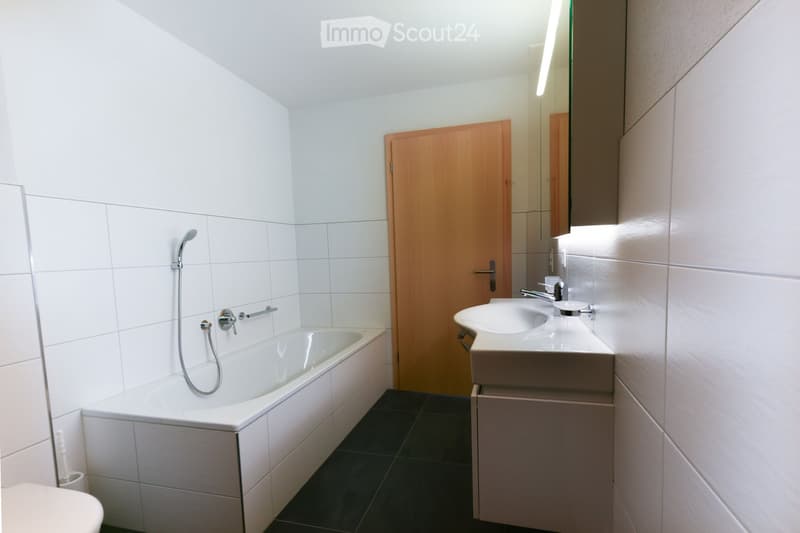 Modern bathroom with white tiled walls, a bathtub with a handheld shower, a sink with a modern faucet, and a mirrored cabinet.