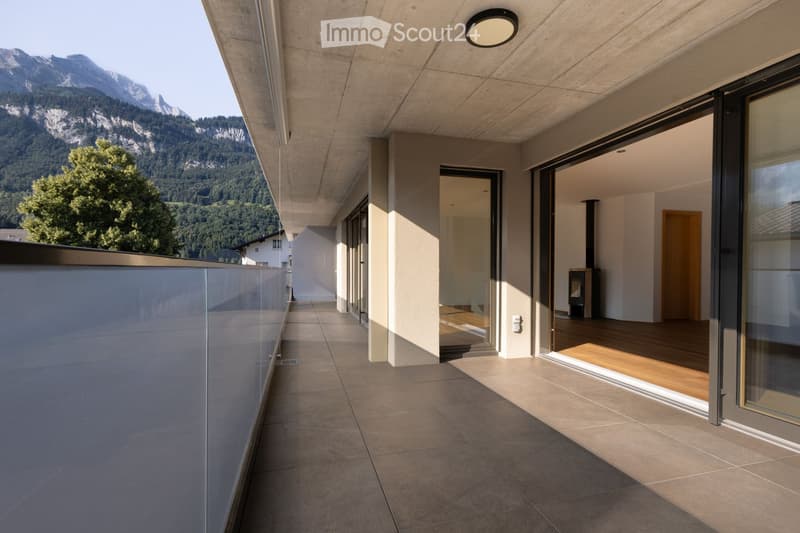 Modern balcony with large glass railings, tiled floor, and scenic mountain view.
