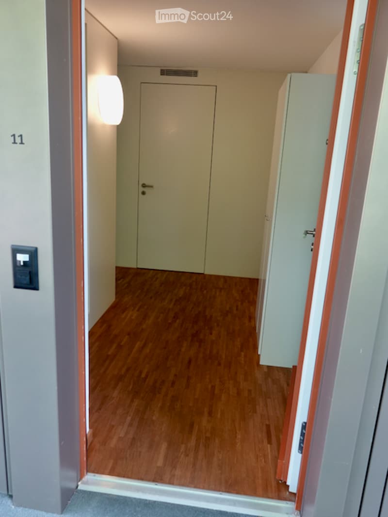 Empty hallway with wooden flooring, white walls, and a closed door at the end.