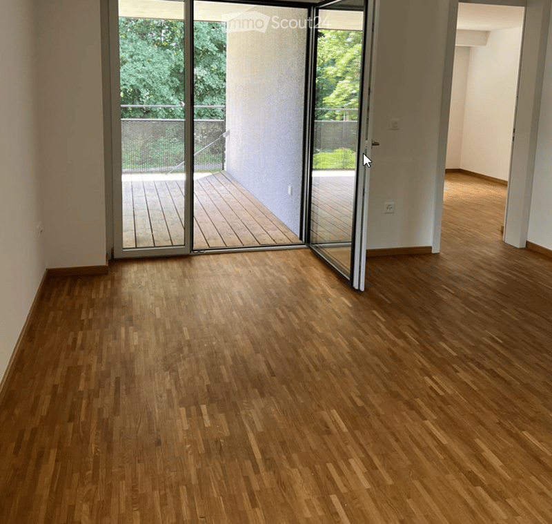 Empty room with wooden flooring and large sliding glass doors leading to a wooden deck and outdoor area.
