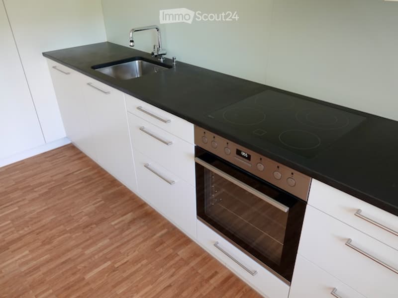 Modern kitchen with white cabinets, black countertops, induction cooktop, oven, and a stainless steel sink.