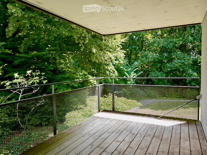 Wooden balcony with metal railing, overlooking a lush green forest.