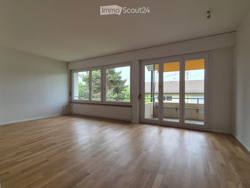 Empty room with wooden flooring, large windows, and sliding glass doors leading to a balcony.