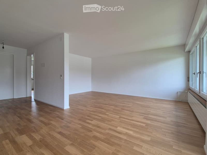 Empty room with light wooden flooring, white walls, and large windows allowing natural light. No furniture or decorations are present.