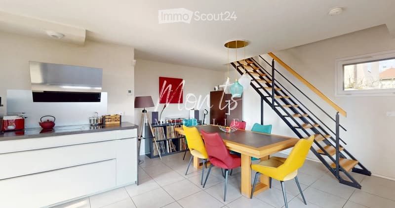 Open-plan kitchen and dining area with modern appliances, a wooden dining table with colorful chairs, and a staircase leading to an upper level.
