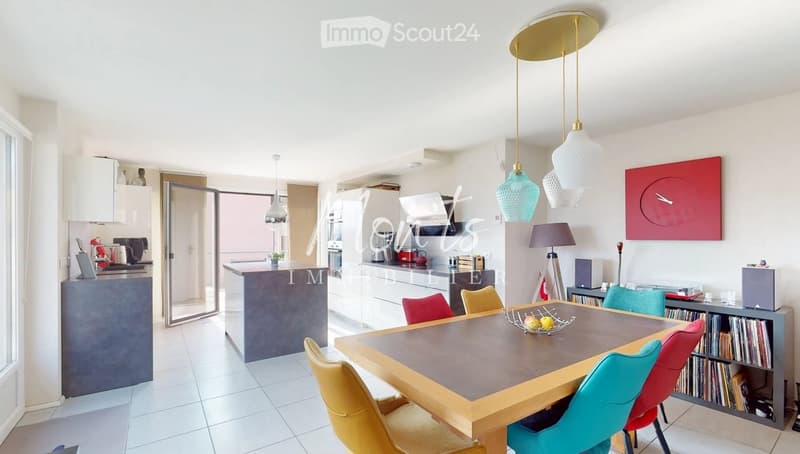 Open-plan kitchen and dining area with modern furniture, pendant lights, and a large dining table surrounded by colorful chairs.