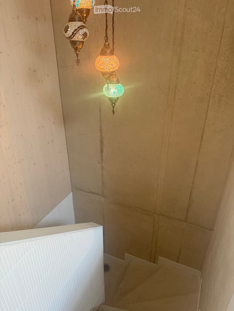 A narrow hallway with beige walls and a white railing, featuring decorative hanging lamps with intricate glasswork.