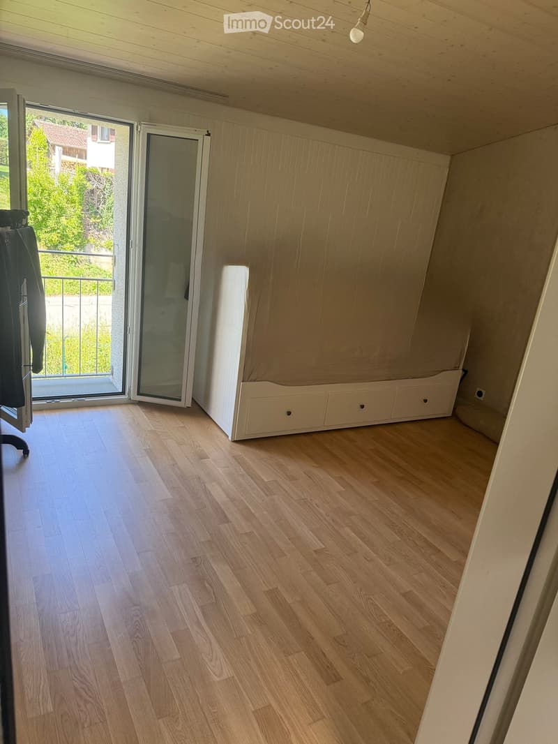 Empty room with wooden flooring, white walls, and a sliding glass door leading to a balcony.