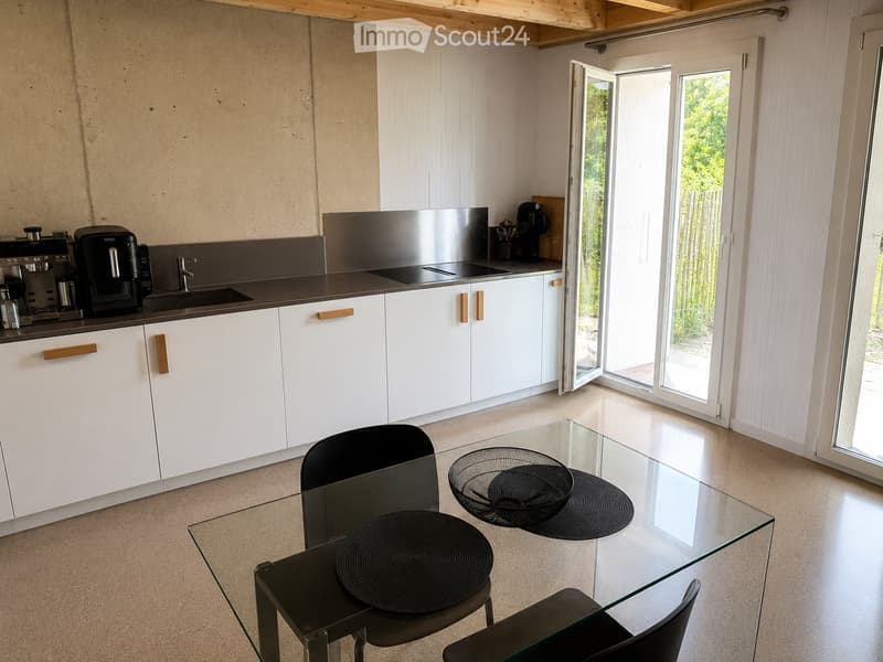 Modern kitchen with white cabinets, stainless steel appliances, and a glass dining table with black chairs.