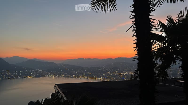 A serene outdoor view at sunset, featuring a calm body of water, distant city lights, and palm trees in the foreground.