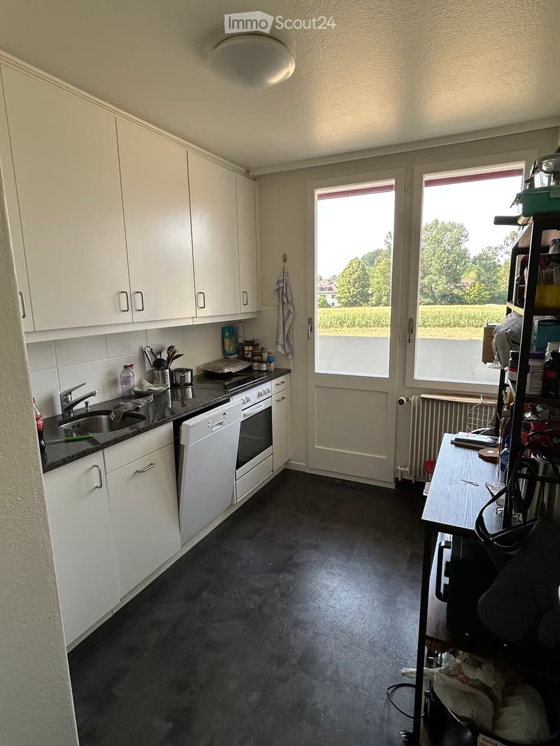Modern kitchen with white cabinets, dark countertops, and stainless steel appliances. Features a sink, oven, dishwasher, and a small table with various items.