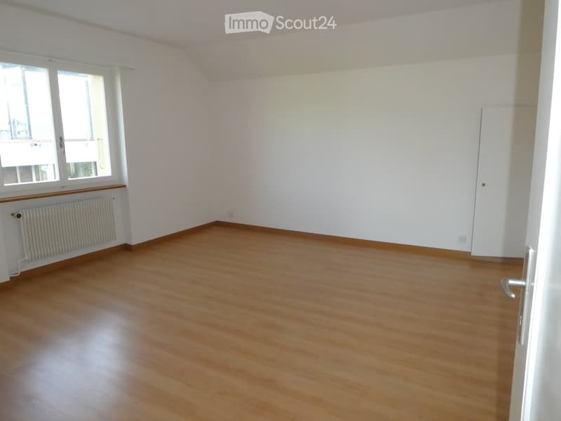 Empty room with wooden flooring, white walls, and a window with a radiator below it.
