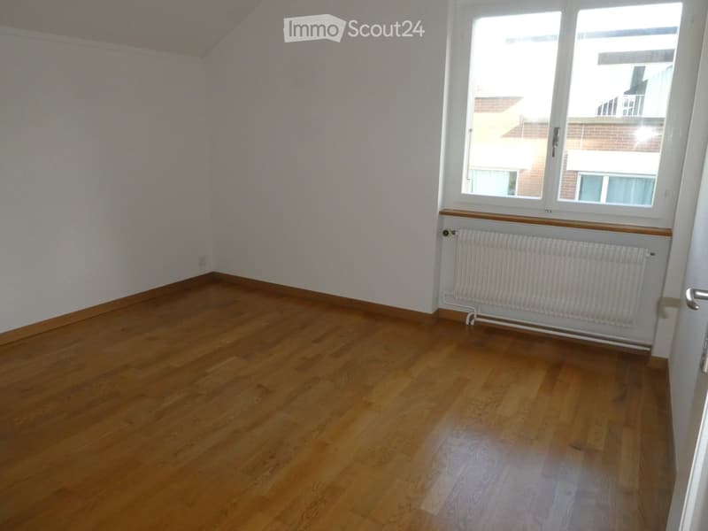 Empty room with wooden flooring, white walls, and a window with a radiator below it.