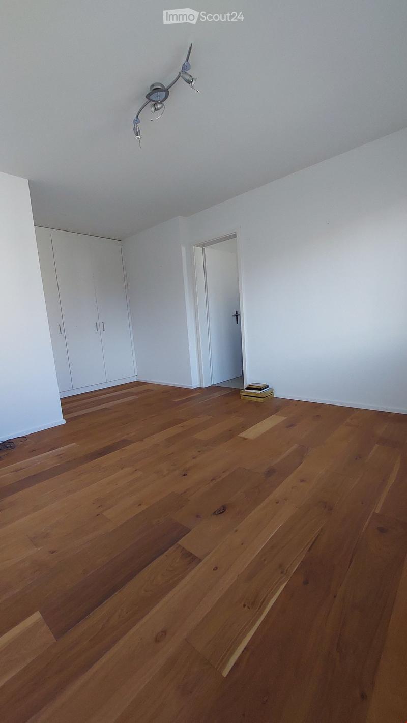 Empty room with wooden flooring, white walls, and a white closet. A small stack of books is placed on the floor near the doorway.