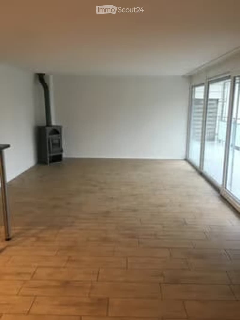 Completely empty room with wooden flooring, white walls, large windows, and a fireplace in the corner.