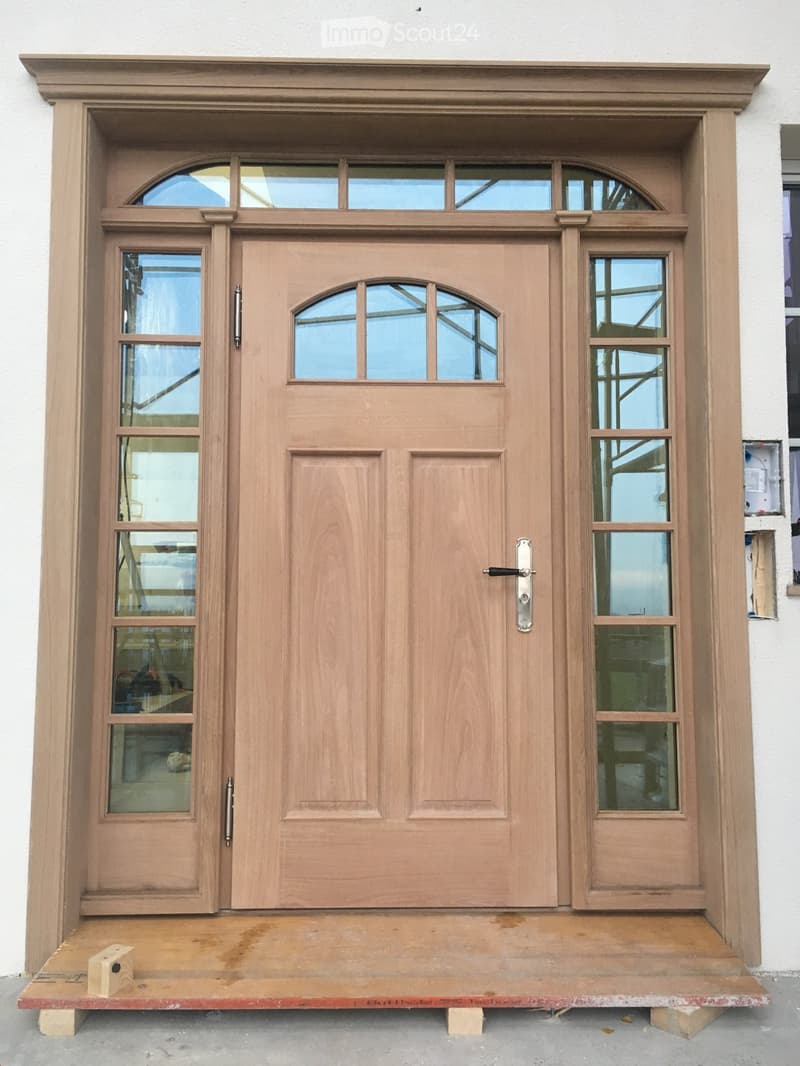 Wooden double door with glass panels, decorative frame, and brass handles, mounted on a wooden platform.