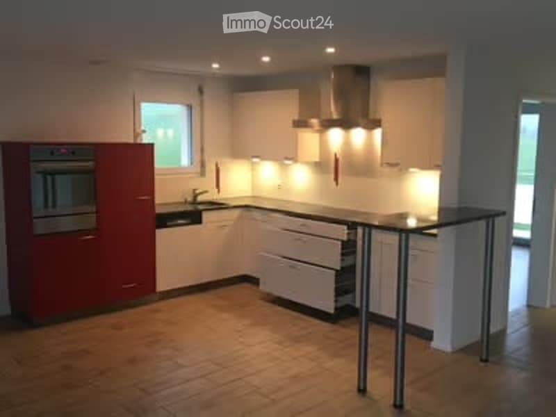 Modern kitchen with white cabinets, red accent wall, central island, built-in oven, and sleek lighting.