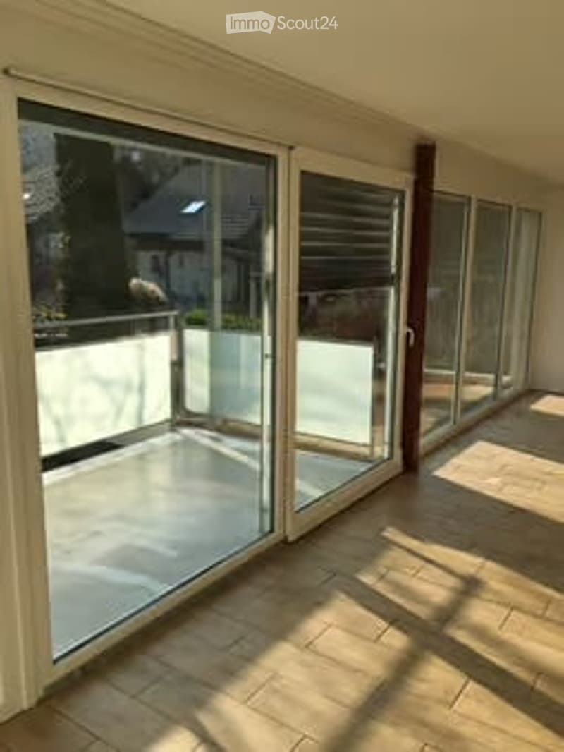 Spacious balcony with large glass sliding doors, tiled floor, and a view of the surrounding area.