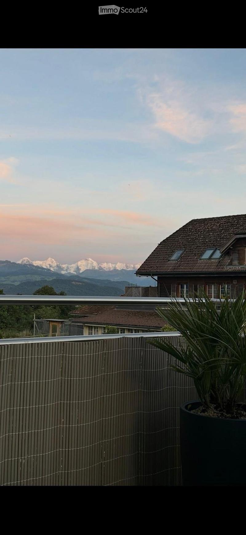 Balcony with a wooden railing, potted plant, and a scenic mountain view in the background.