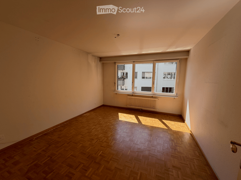 Empty room with wooden flooring, white walls, and a large window with a radiator below it.