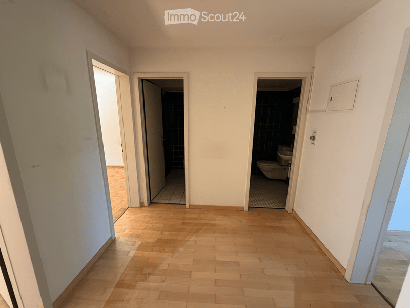 Empty hallway with wooden flooring, white walls, and two open doors leading to bathrooms.