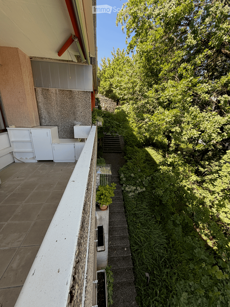 Balcony with tiled floor, white cabinets, and a view of a lush garden with various plants and trees.