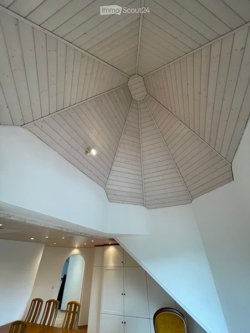 Dining area with a wooden dining table, chairs, and built-in cabinets under a slanted wooden ceiling with recessed lighting.