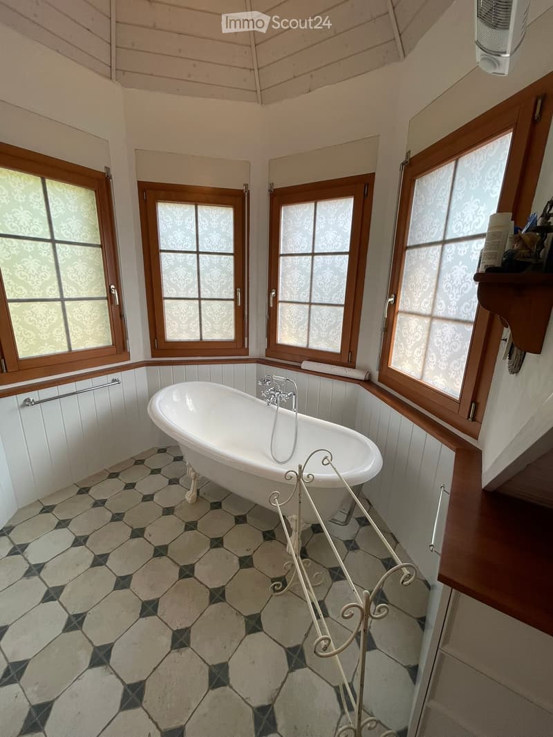 Bathroom with a white clawfoot bathtub, decorative tile floor, wooden windows with frosted glass, and a towel rack.