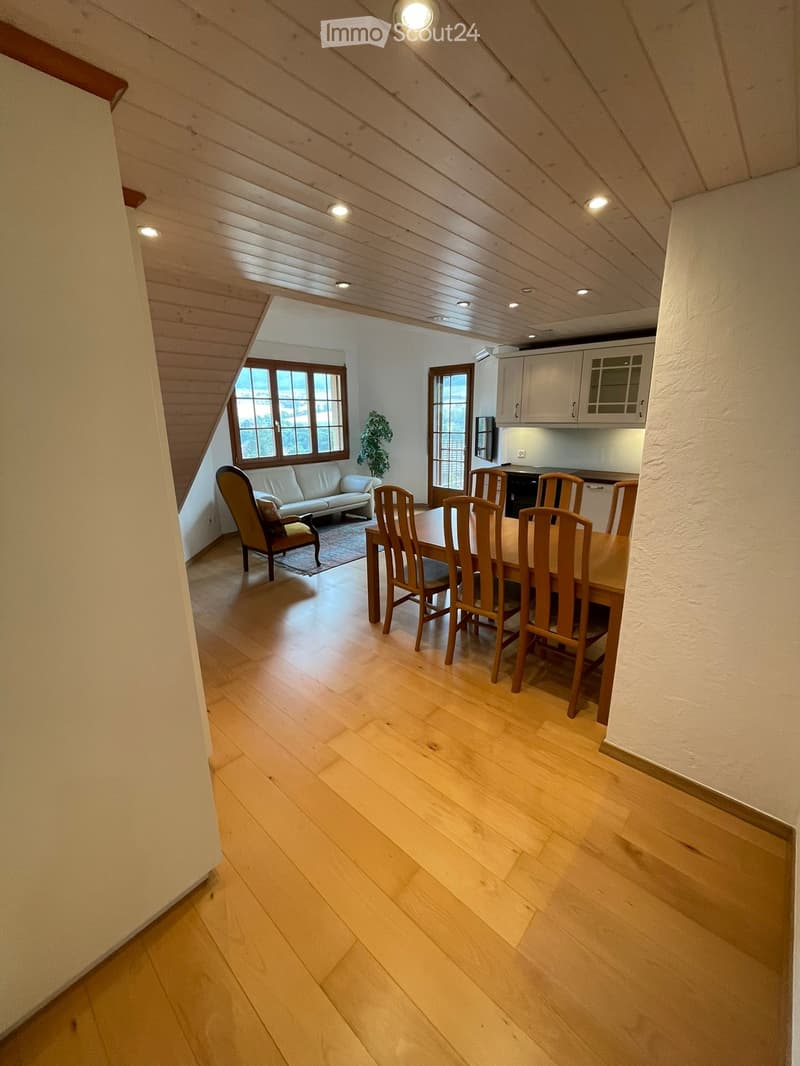 Open-plan living and dining area with wooden flooring, a white sofa, a dining table with chairs, and a small kitchen area with cabinets.